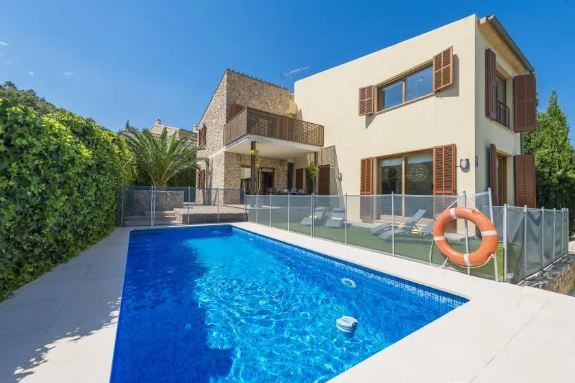 A swimming pool beside a modern house, with a glass fence and an orange lifebuoy.