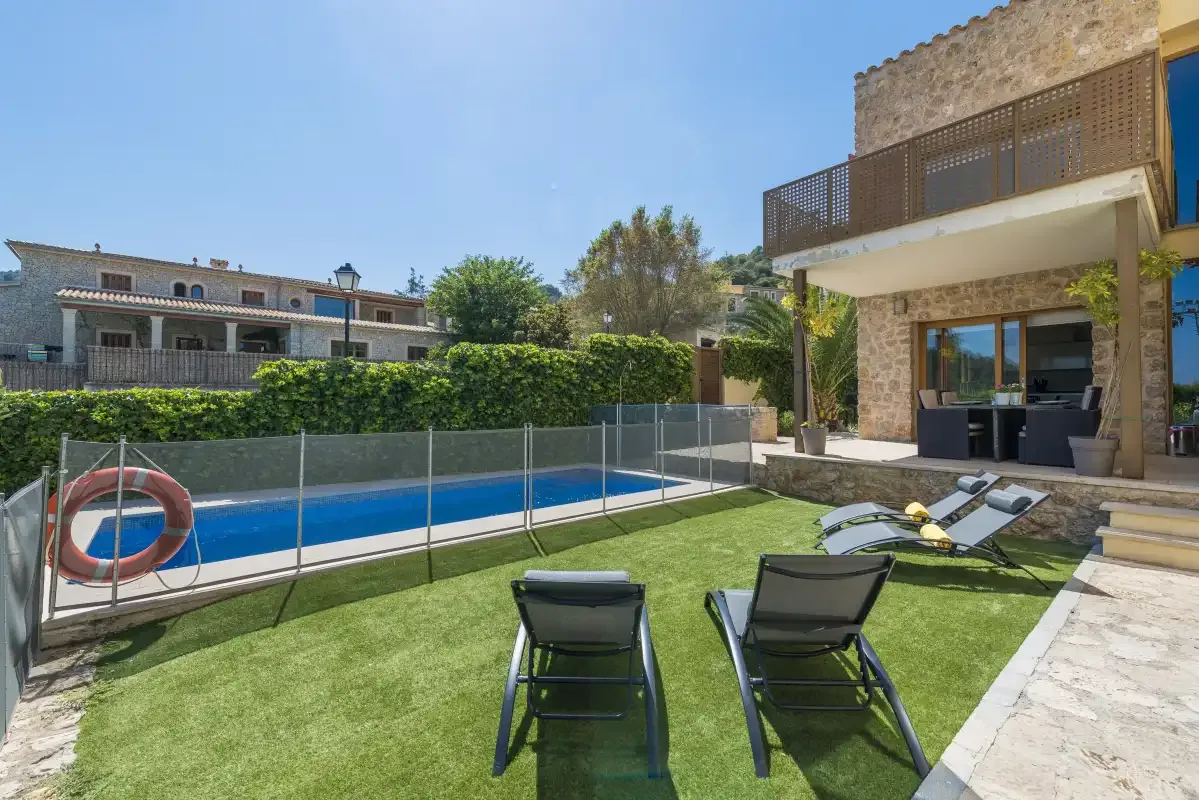 A poolside patio with a lawn, lounge seating, and a stone-clad house.