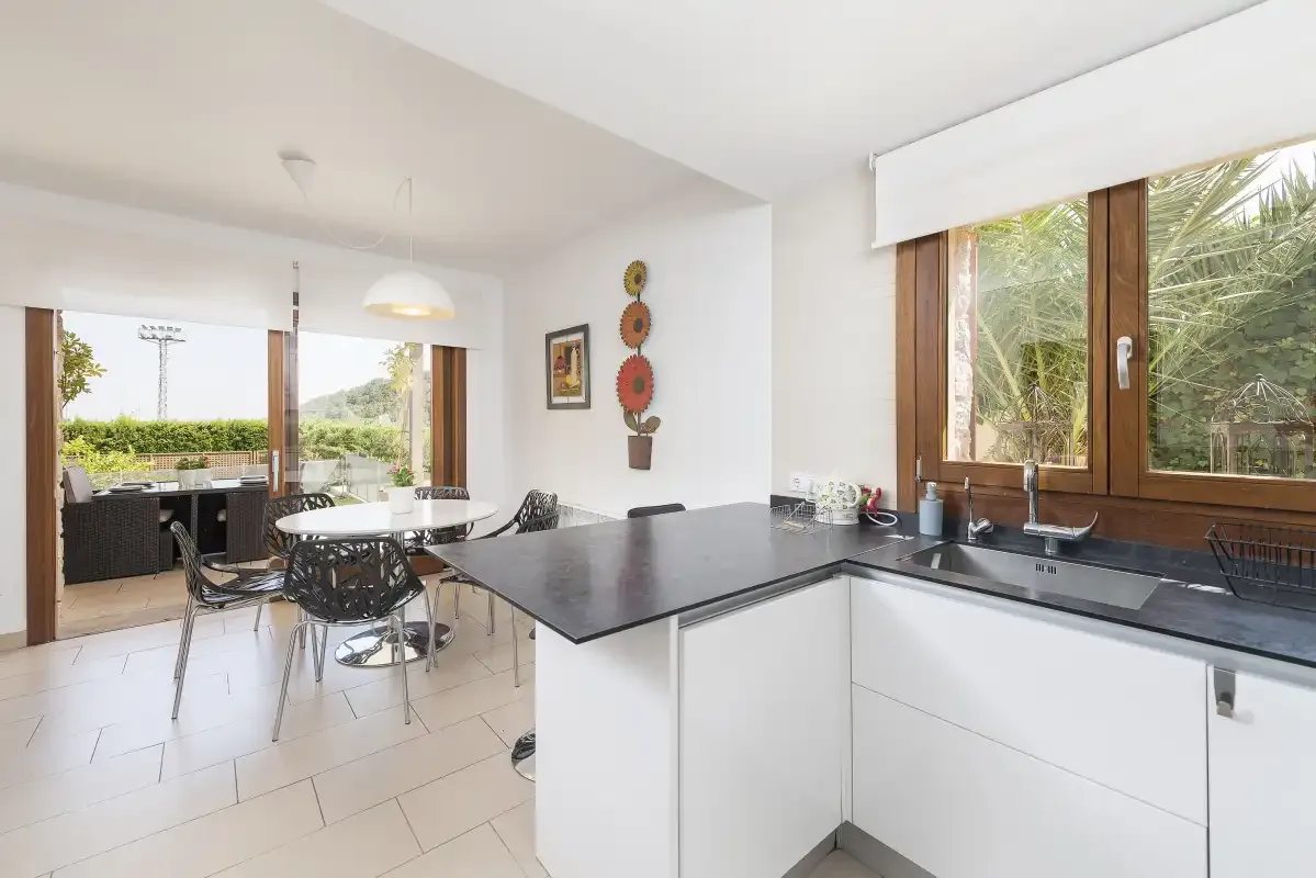 A bright kitchen opens onto a dining area beside large windows.