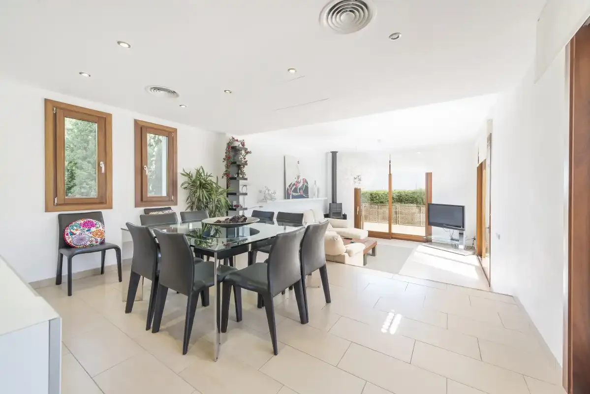 A bright dining and living room with a glass table and sliding doors.