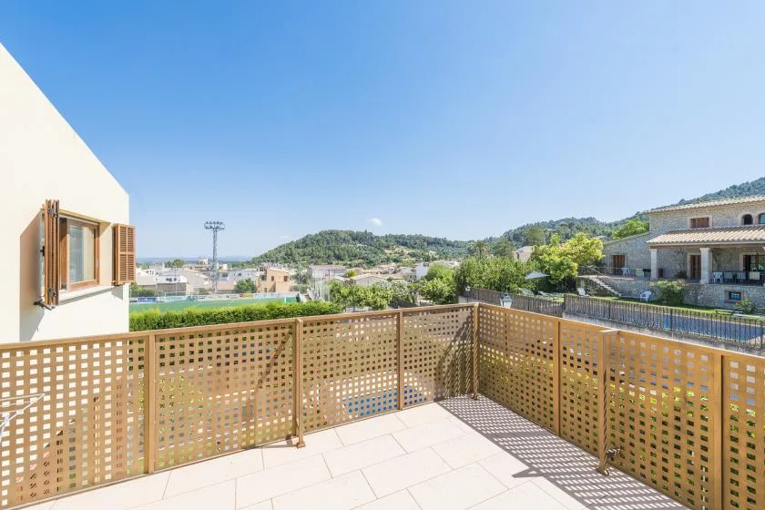A sunny balcony overlooks nearby buildings and green hills.