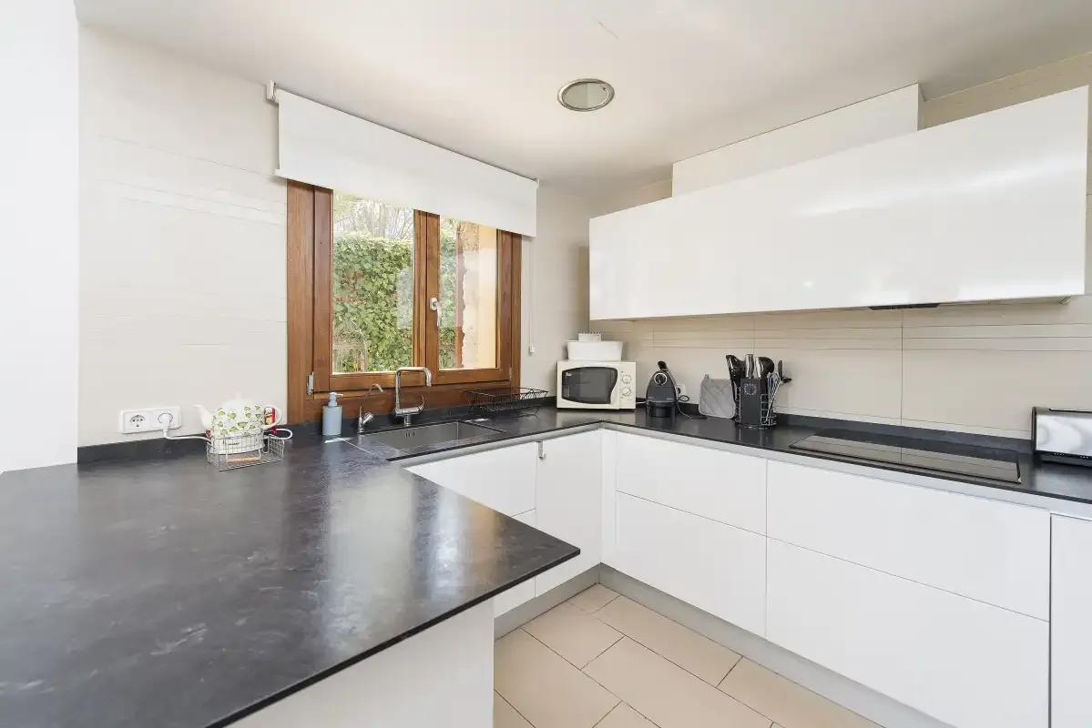 A modern kitchen with white cabinets, dark countertops, and a window.