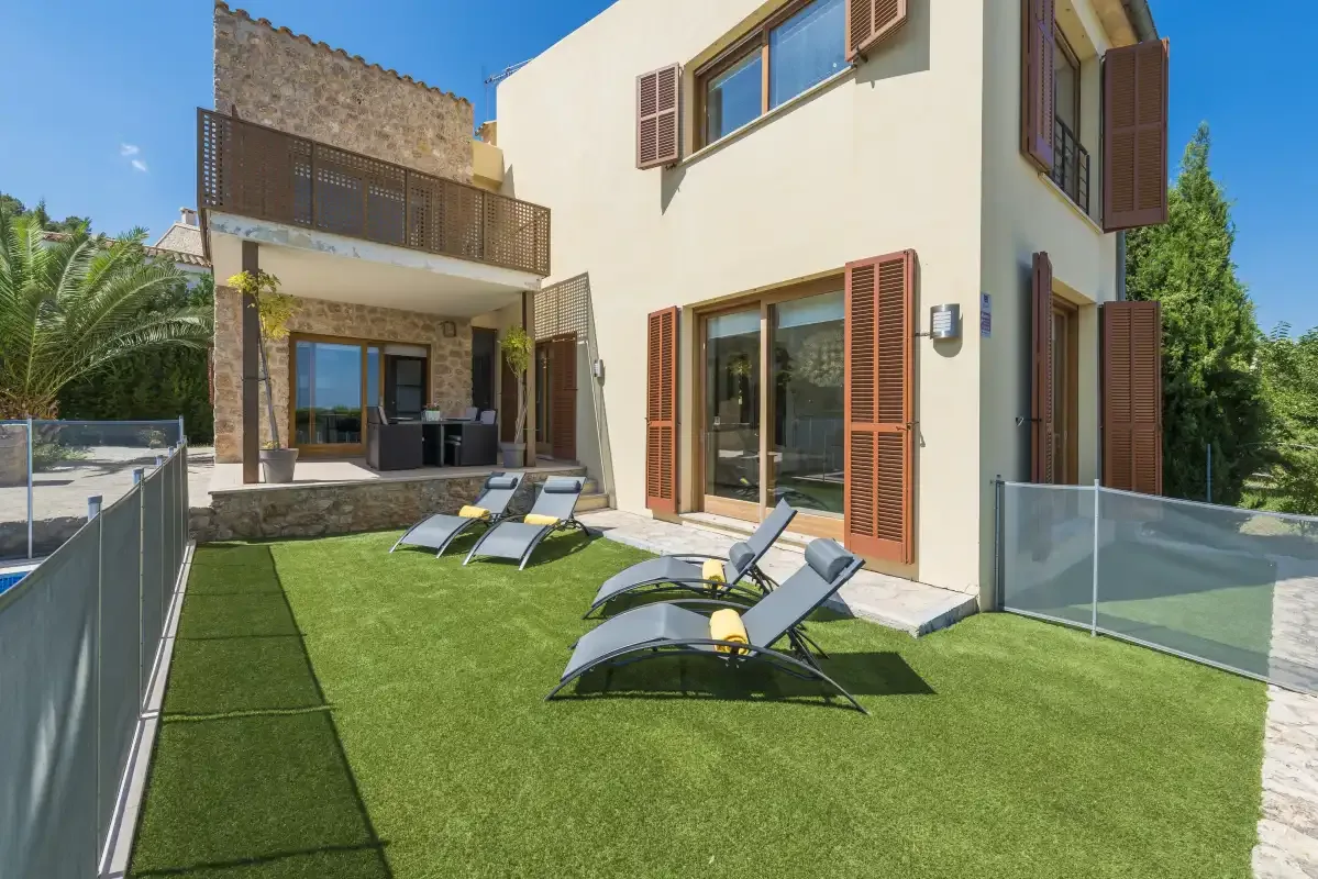 A sunny courtyard beside a house has a lawn and outdoor loungers.