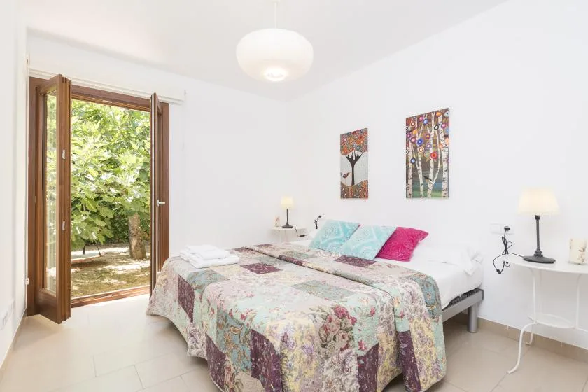 A bright bedroom with a double bed and an open door to greenery.
