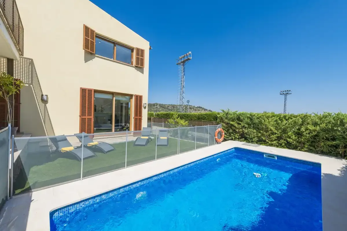 An outdoor swimming pool beside a modern building and a glass-railed patio.