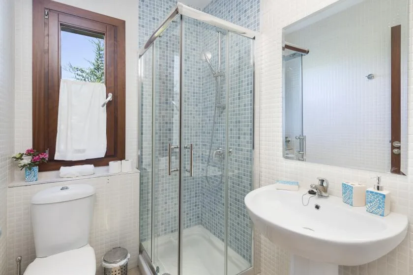A bright bathroom with a glass shower, sink, and toilet.