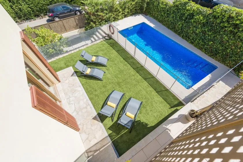 An outdoor swimming pool beside a rectangular lawn with lounge seating.