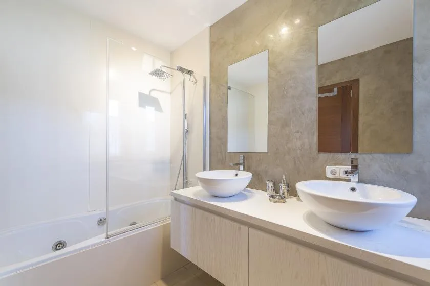 A bright bathroom with a bathtub, glass shower screen, and double sinks.