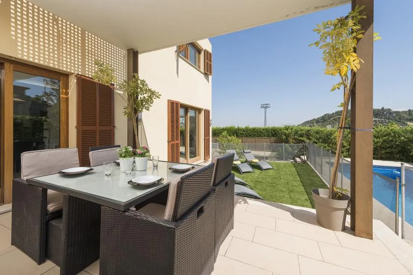 A covered outdoor dining area overlooks a small lawn and swimming pool.