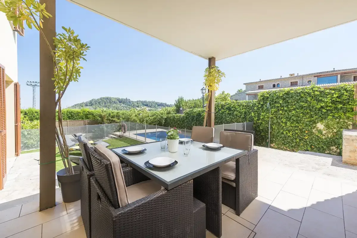 A covered outdoor dining area with a table and seating overlooks a garden.