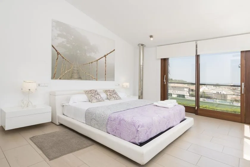 A bright bedroom with a bed beside large windows overlooking the outdoors.