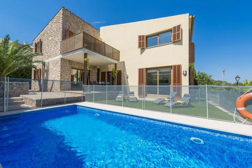 A swimming pool sits beside a modern house with a fenced patio.
