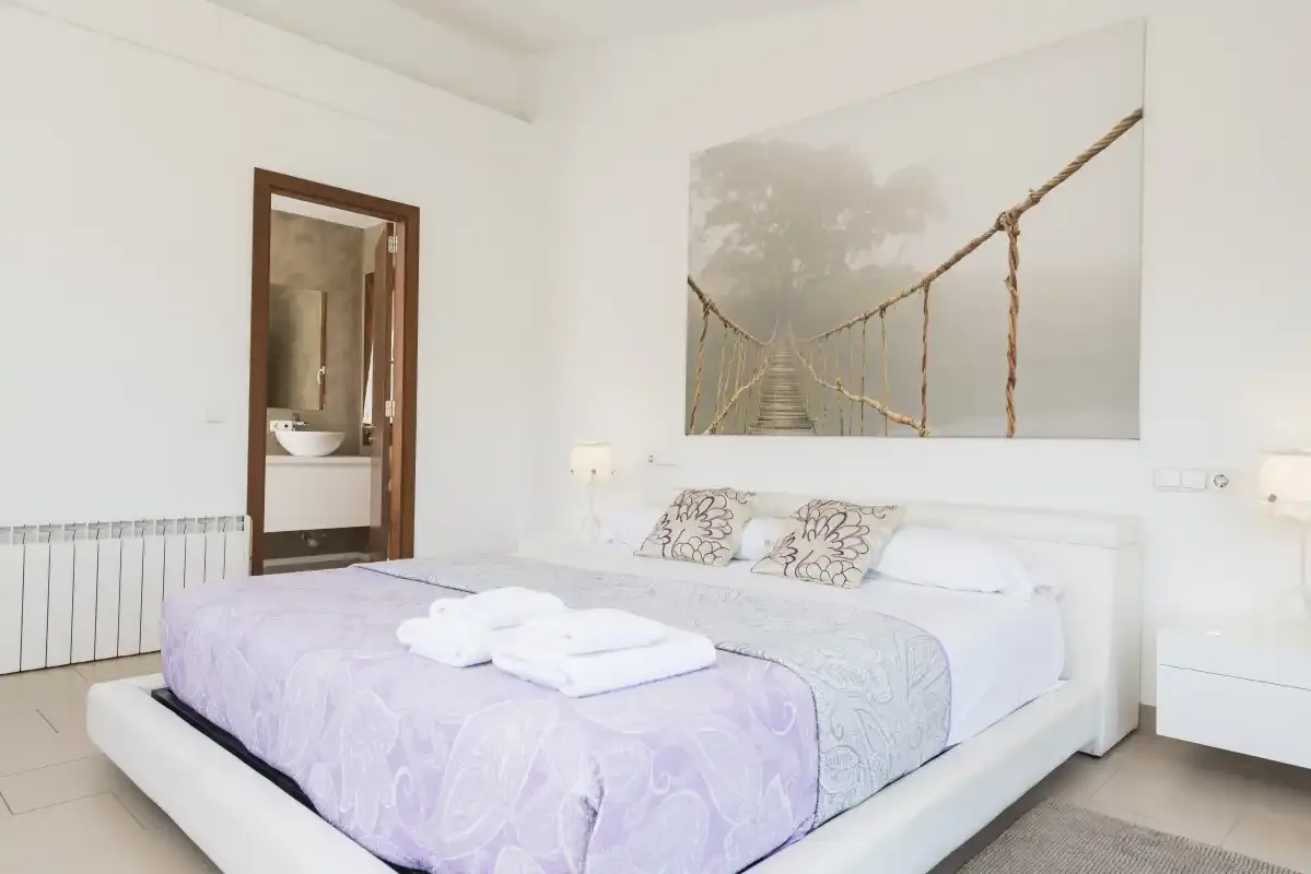 A bright bedroom with a bed and a large wall picture.