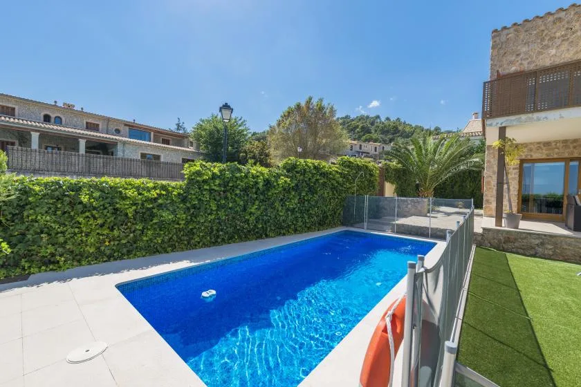 A blue swimming pool sits beside a hedge and a modern building.