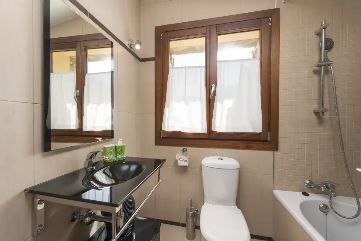 A tiled bathroom with a sink, toilet, and bathtub beneath a window.