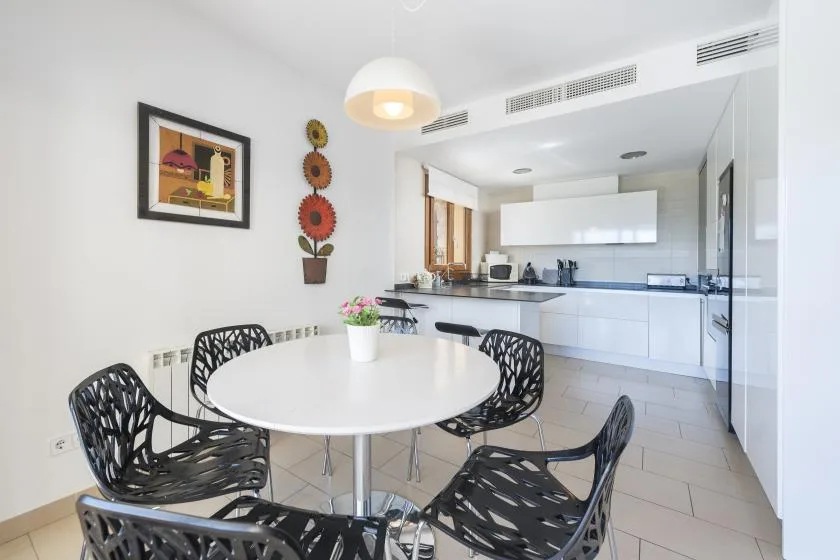 A bright dining area with a round table and an open kitchen beyond.
