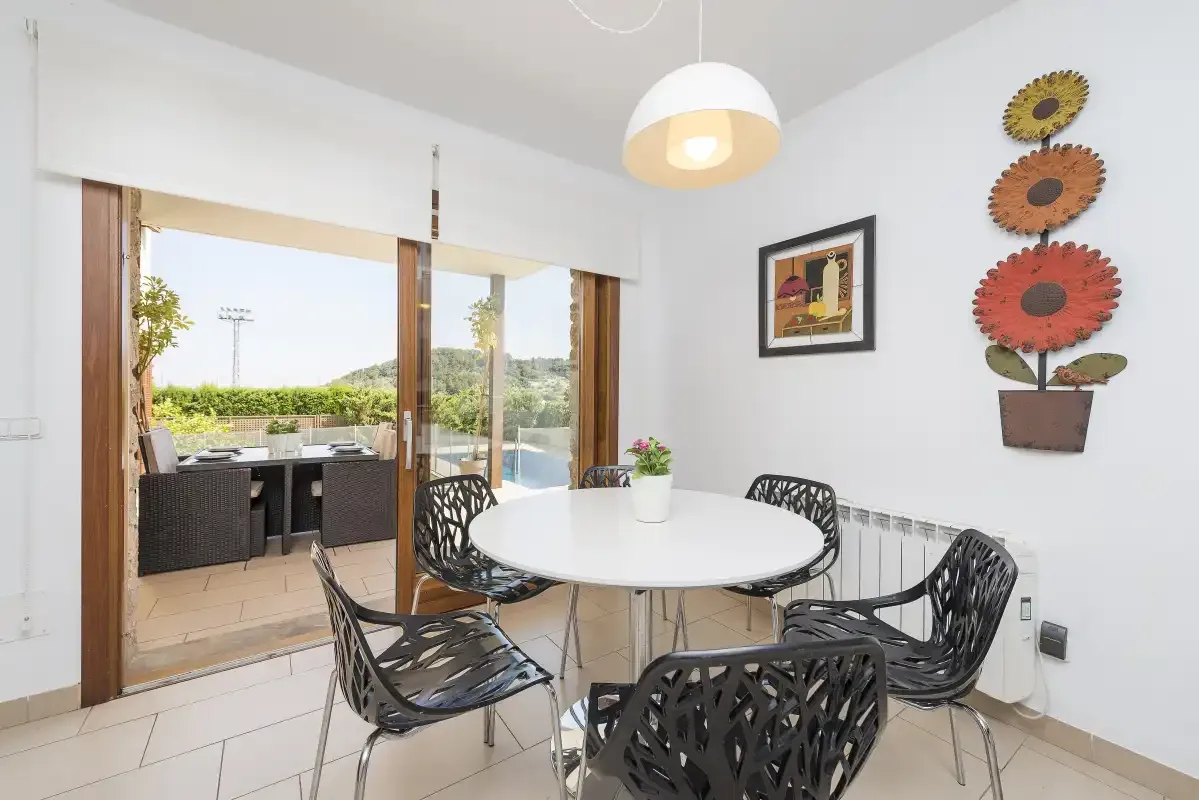 A dining area with a round table and black chairs beside an open patio door.