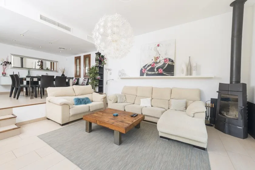 A bright living room with sectional seating, a wooden coffee table, and a freestanding fireplace.