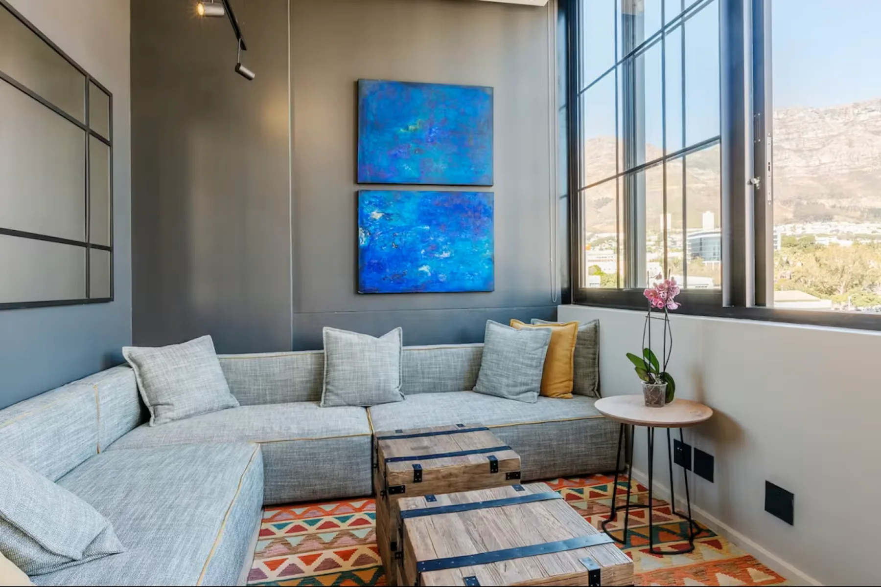 A bright living room with sectional seating, colorful wall art, and large windows.