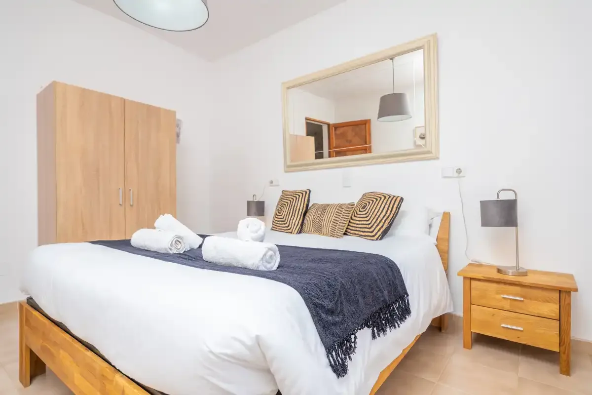 Un dormitorio con una cama bien tendida, toallas dobladas y un armario de madera.
