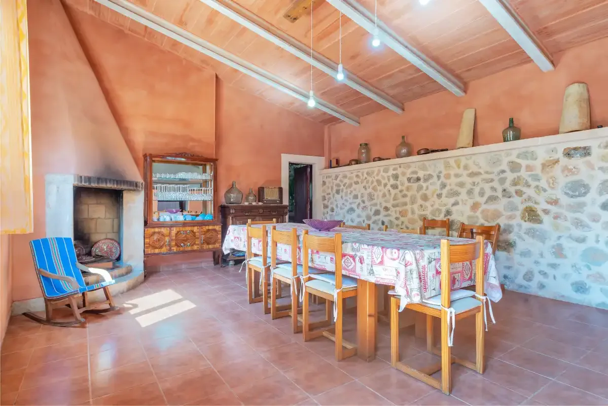 Un comedor con una mesa larga, sillas y una pared de piedra.