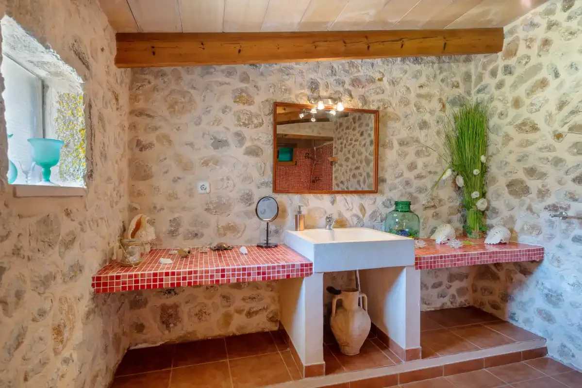 Un baño con paredes de piedra, lavabo, espejo y encimera de azulejos.