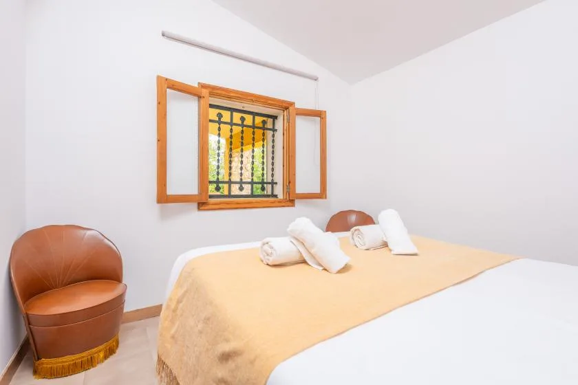 Un dormitorio con una cama cubierta con una manta amarilla y una ventana con contraventanas de madera abiertas.