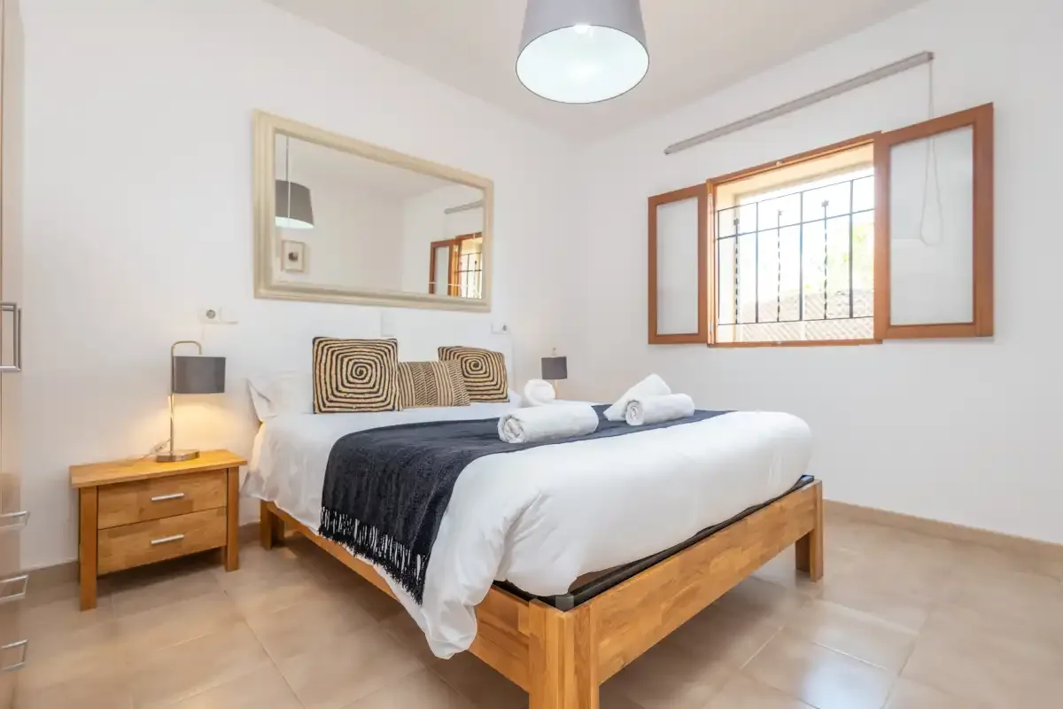 Un dormitorio luminoso con una cama de madera y una ventana abierta.