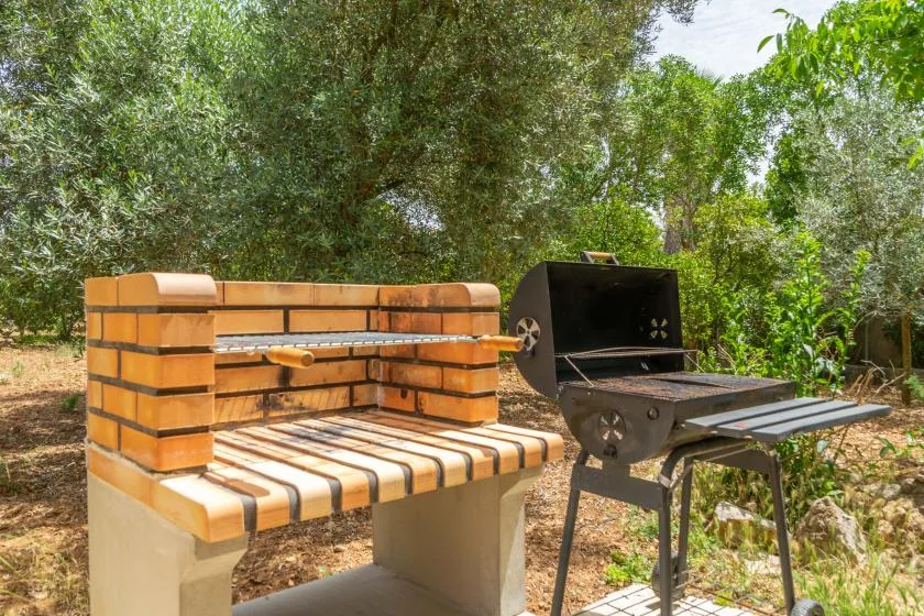 Una zona de cocina al aire libre con una barbacoa de ladrillo y una parrilla metálica entre árboles.