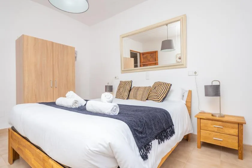 Un dormitorio con una cama bien arreglada, cojines estampados y una mesita de noche de madera.