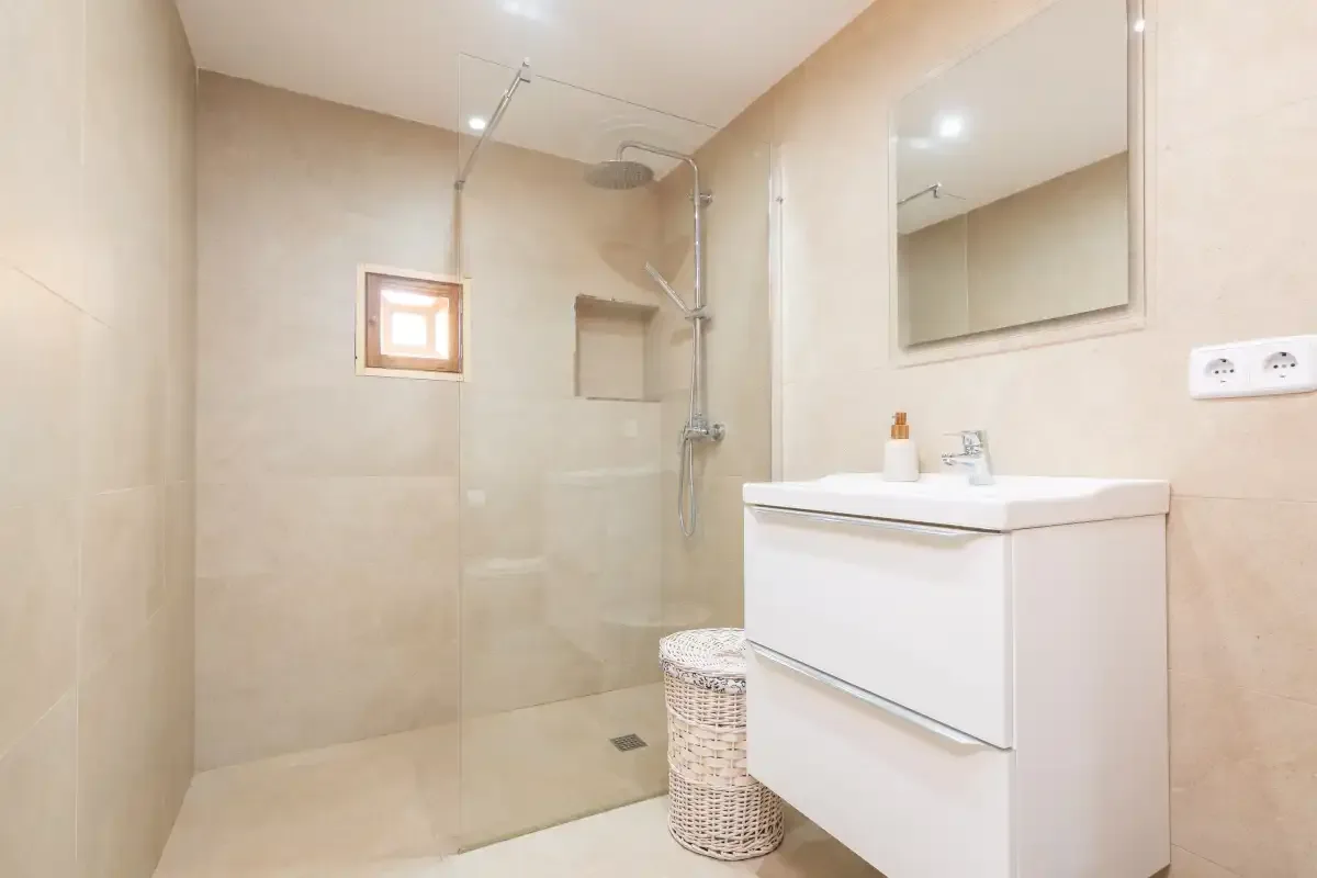 Un baño luminoso con ducha y un mueble lavabo blanco.