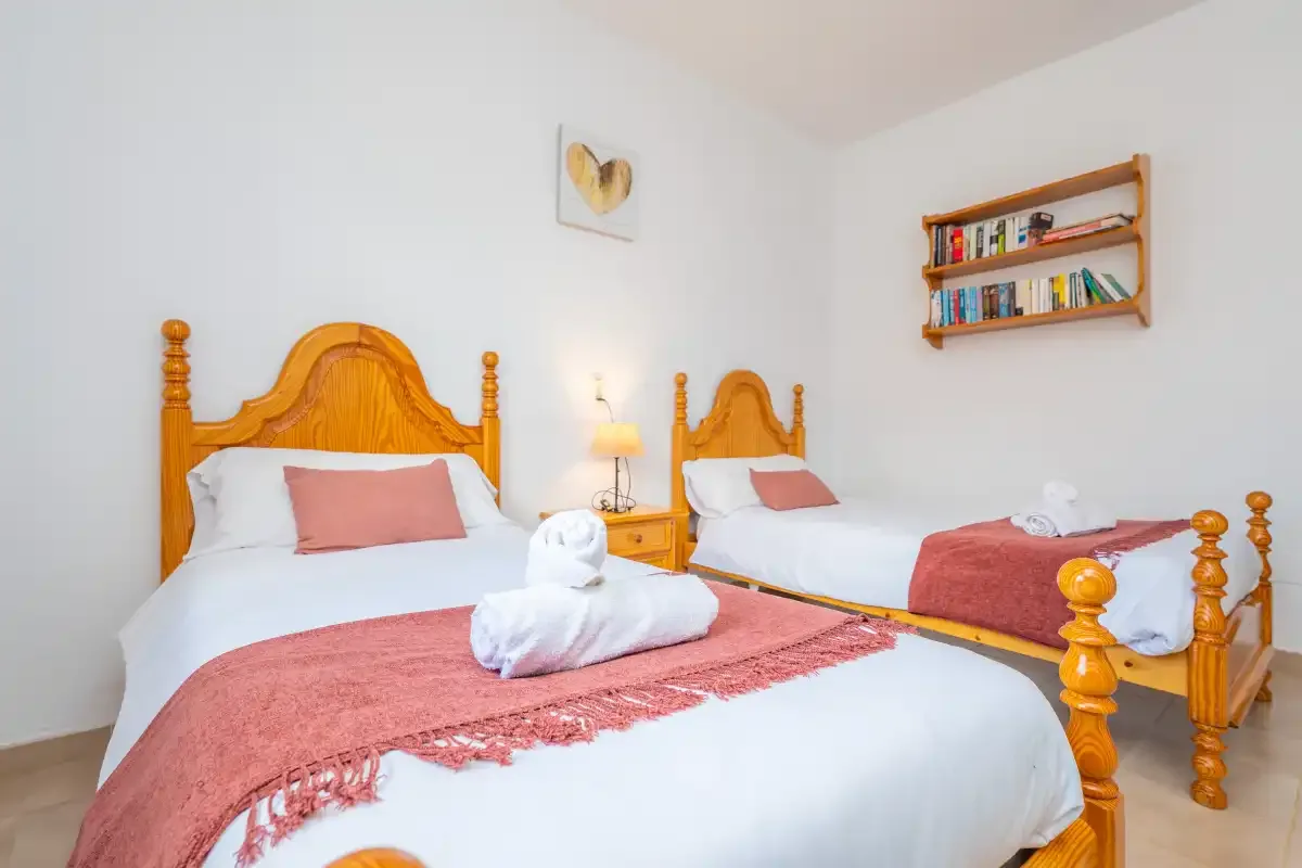 Un dormitorio con dos camas, ropa de cama blanca y colchas rojas.