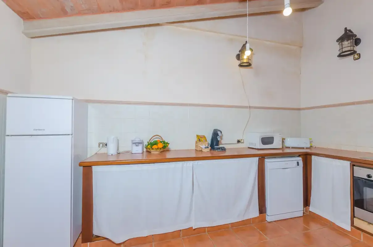 Una cocina con encimeras de madera, electrodomésticos y suelo de baldosas color terracota.