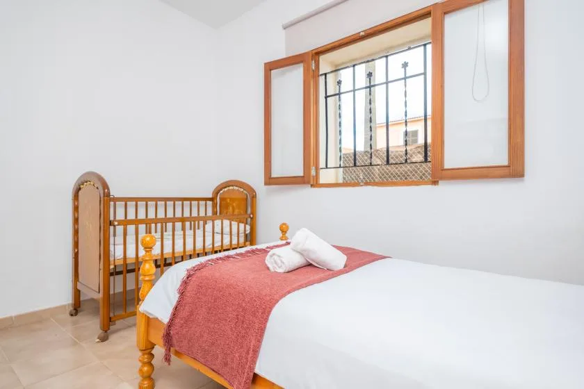Un dormitorio luminoso con una cama de madera y una ventana con barrotes.