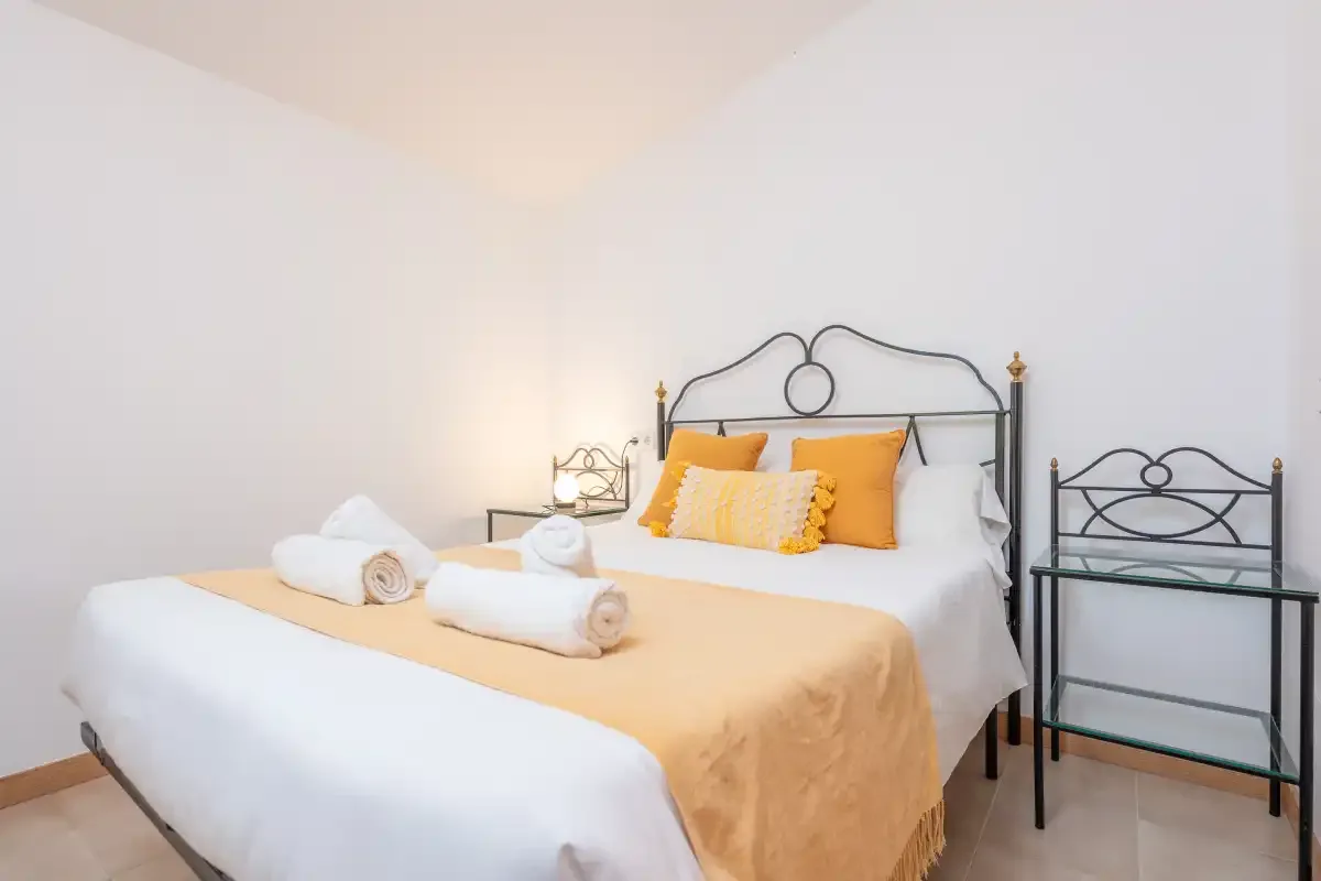 Un dormitorio con una cama tendida y almohadas naranjas.
