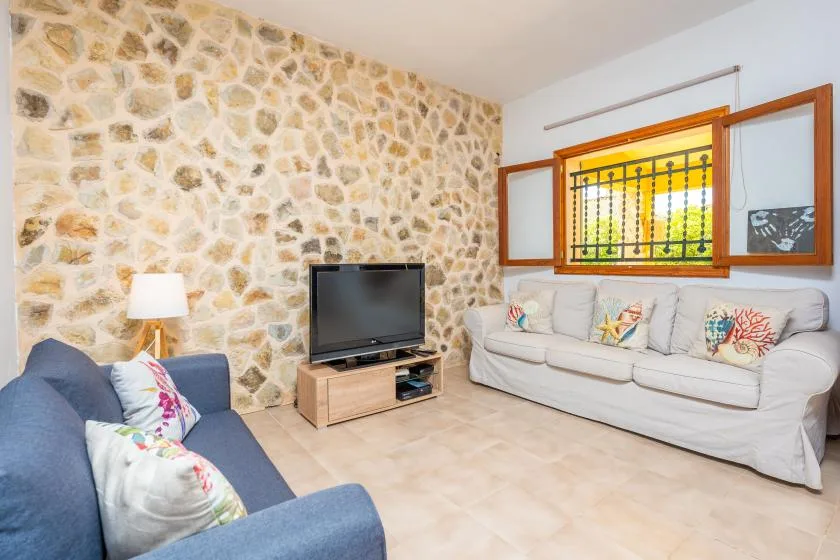 Una sala de estar con asientos, un televisor y una ventana con contraventanas abiertas.