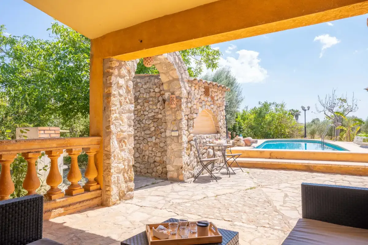 Un patio cubierto de piedra con asientos al aire libre da a una piscina.