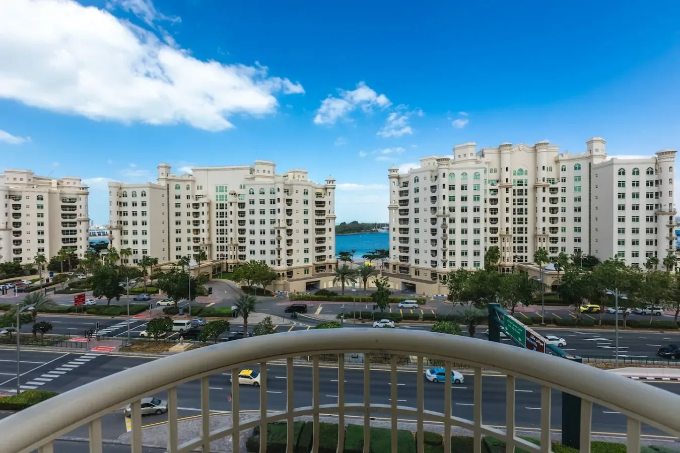 A balcony overlooks residential buildings, roads, and a strip of water under a blue sky.