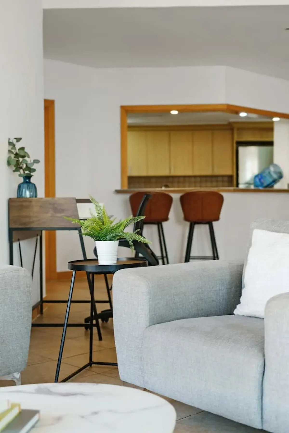 A living room with light-colored seating and a small table beside a kitchen counter.