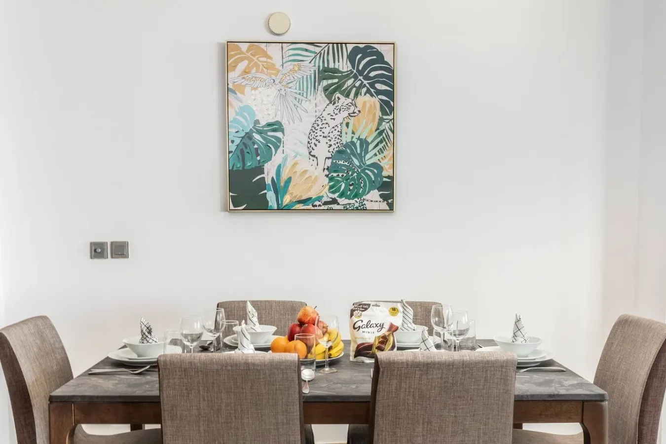 Un comedor con la mesa puesta bajo un cuadro botánico colorido.