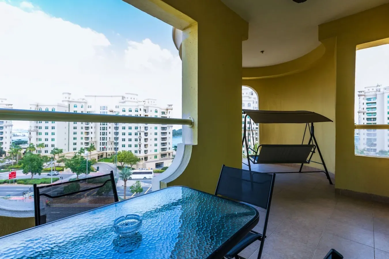 A balcony seating area with a glass table overlooks nearby buildings.
