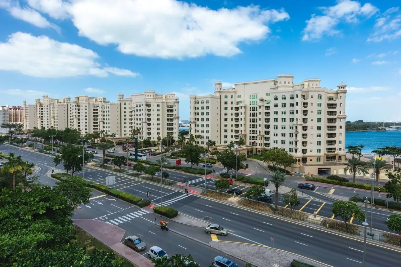 A coastal city view shows apartment buildings beside a multilane road and the sea.