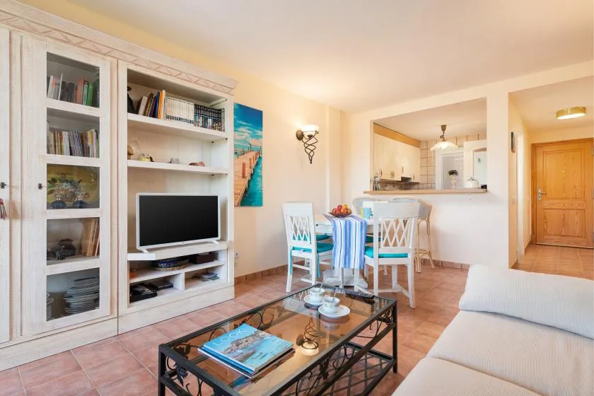 A bright living room with a television, dining table, and open kitchen.
