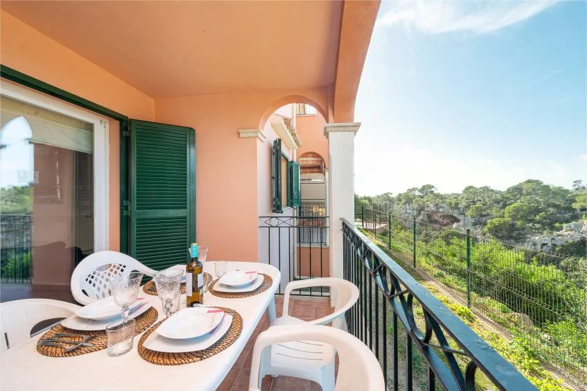 A covered balcony with a dining table and chairs overlooks green treetops.
