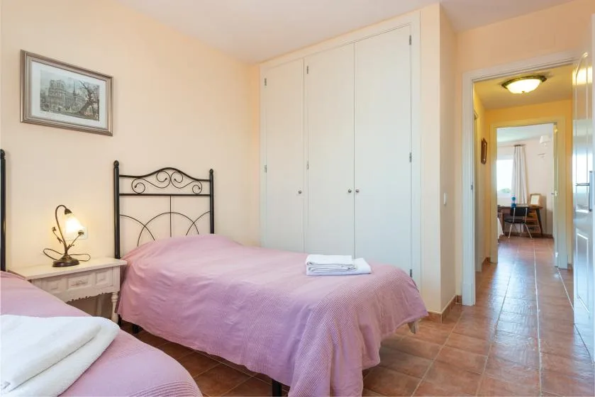A bedroom with pink bedding, a bedside table, and a white wardrobe.