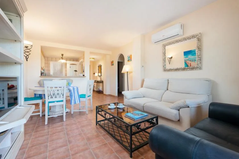 A bright living room with a light-colored sofa, coffee table, and adjoining dining area.