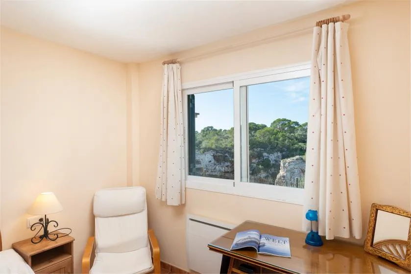 A sitting room with a window overlooking trees and a desk by the window.