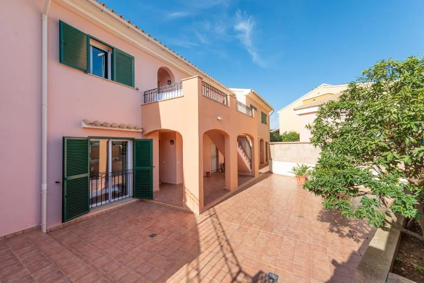 A tiled courtyard beside a pink building with arched openings and green shutters.