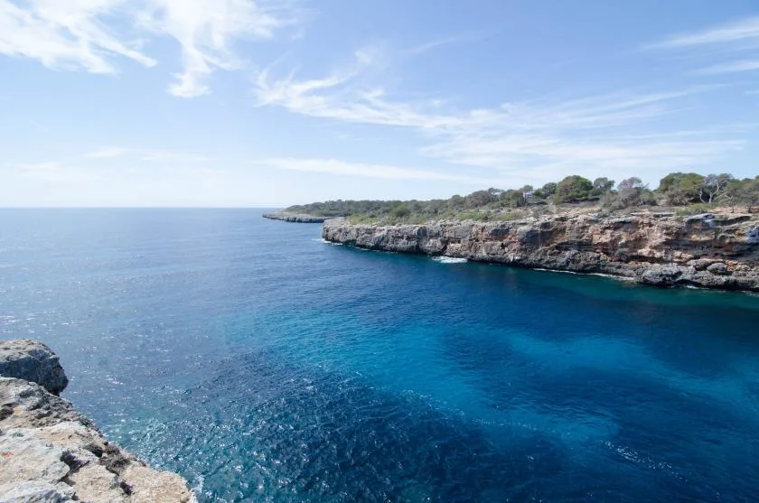A coastal cove with clear blue water and rocky cliffs beneath a bright sky.