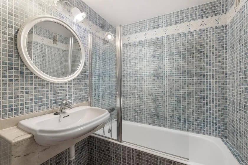 A tiled bathroom with a sink, round mirror, and bathtub.